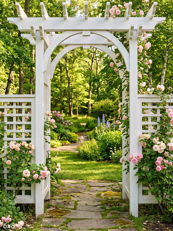 White pergola arbor between lattice fence panels with climbing pink and cream roses over a flagstone garden path, a photography backdrop.