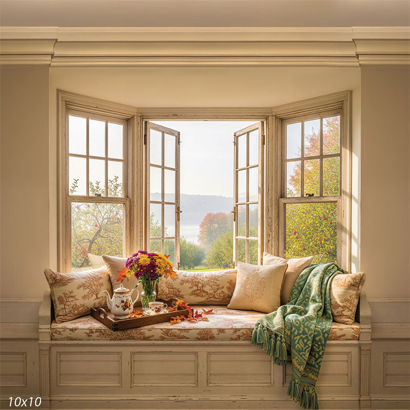 A cozy window seat backdrop featuring soft cushions, a warm blanket, and a scenic autumn view, ideal for intimate fall portraits.