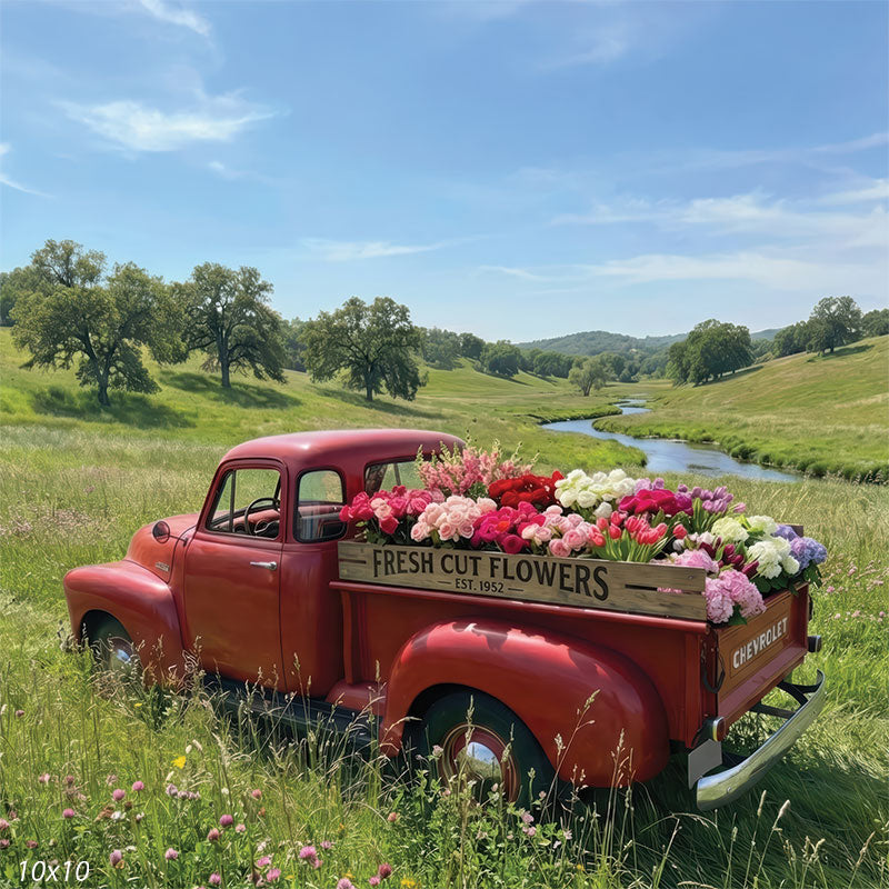 Photography backdrop featuring a red truck bed with a fresh cut flowers sign. Tall grass and wildflowers surround the vehicle in a sunlit field.