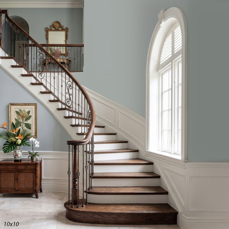 Wider view of the coastal staircase showing the full arched window, a console with a tropical floral arrangement and the upstairs landing, a coastal interior photography backdrop.