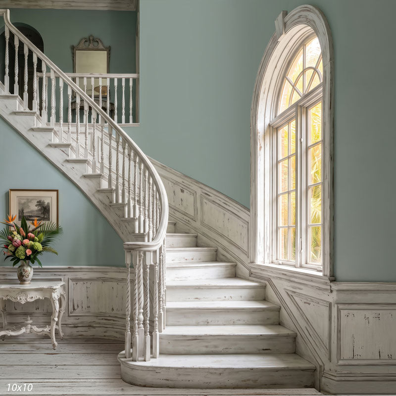 Wider view of the whitewashed staircase showing the full arched palm-view window, a distressed console with a tropical arrangement and the upstairs landing, a coastal interior photography backdrop.