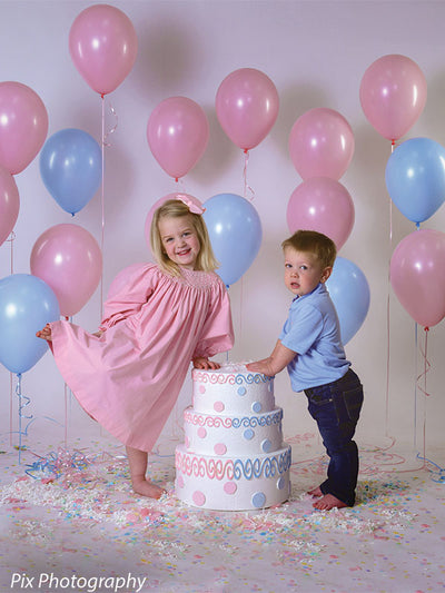 Young girl and boy pose in birthday scene with pastel balloons and cake, all set against seamless gray backdrop.