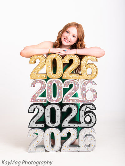 Senior leans cheerfully over a glitter-stacked 2026 number prop, adding sparkle and structure to graduation milestone photography.
