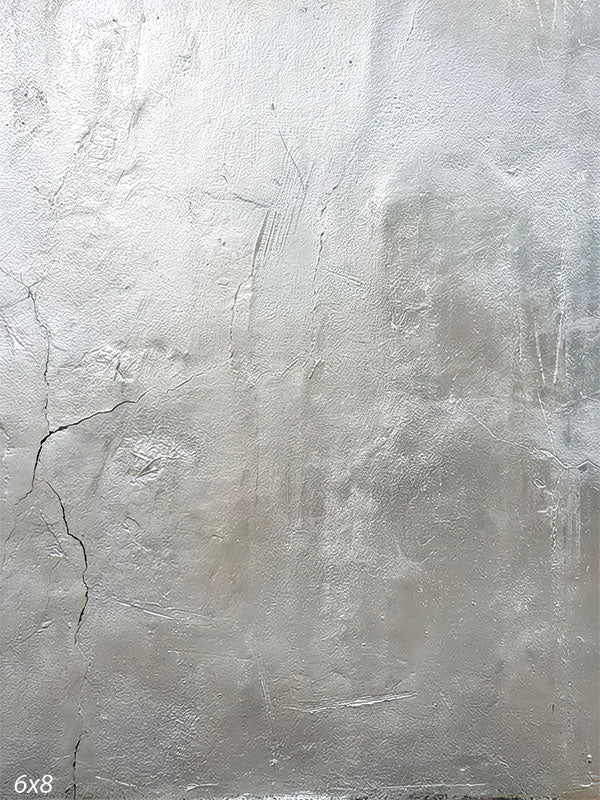 A silver-gray photography backdrop with a softly weathered plaster look, subtle trowel texture, and a faint vertical crack along the left side.