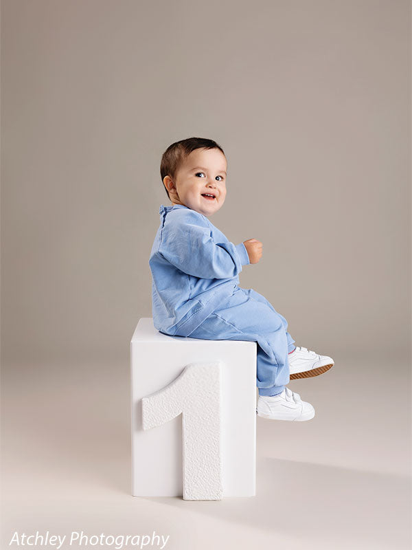 Toddler portrait on milestone prop with neutral gray studio backdrop—ideal for newborn and family studios.
