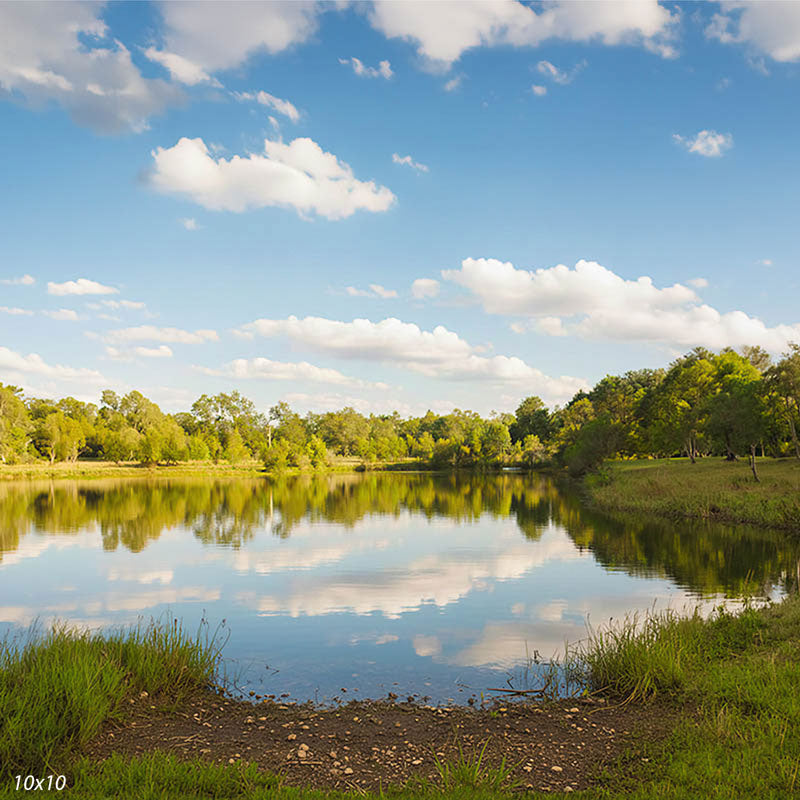Wider view of the lake showing more of the cloud-filled sky, tree line, and grassy shoreline reflected in still water, an outdoor photography backdrop.