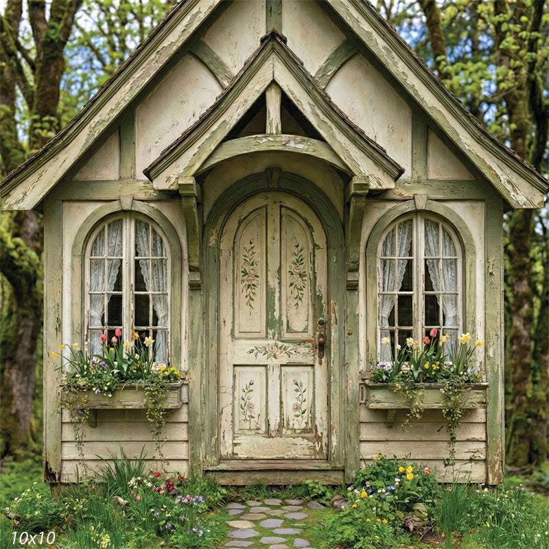Studio background featuring a weathered cottage front with a peaked roof, arched door, window flower boxes, and woodland surroundings for portrait photography.