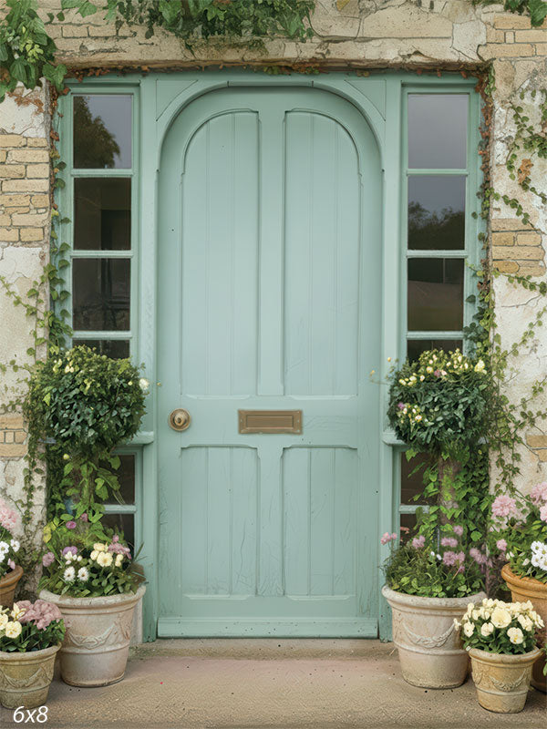 A photography backdrop showing a muted teal cottage door with side windows, climbing vines, and potted flowers arranged at the base. The scene presents a rustic garden entrance suitable for studio backgrounds.