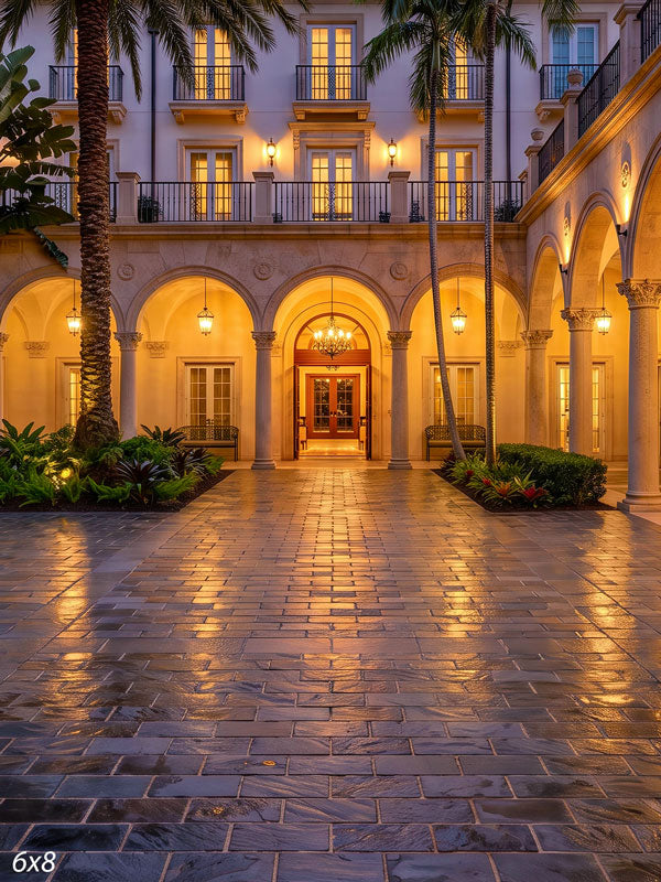 Symmetrical arched colonnade around a tiled courtyard with hanging lanterns, a chandelier, and palms at dusk, a scenic photography backdrop.