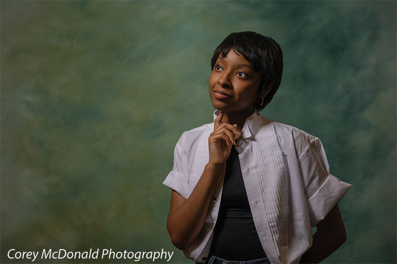 Green abstract hand-painted photography backdrop shown in a wide studio senior portrait with a young woman posed thoughtfully, a hand near her chin OM-2644