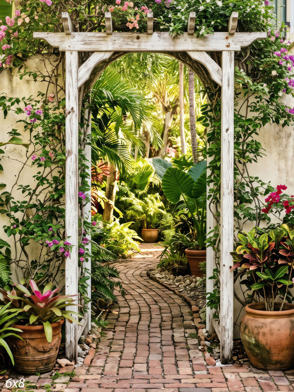 Whitewashed wood arbor draped in pink bougainvillea opening onto a tropical garden with a curved brick path, a scenic photography backdrop.