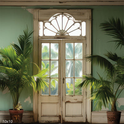 A vintage-style photography backdrop featuring a beautifully weathered double-door with glass panes, framed by lush tropical greenery and palm fronds.