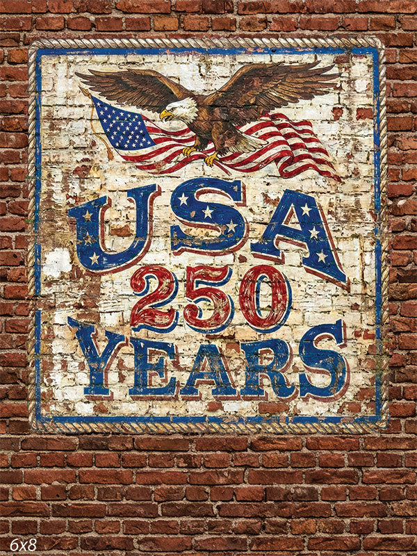 Printed photography backdrop showing a red brick wall with a distressed mural of an eagle, American flag, and USA 250 Years lettering. The studio background has a vintage painted appearance with weathered patriotic graphic details.