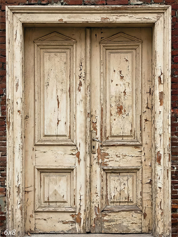 This photography backdrop shows distressed cream-colored double doors with peeling paint set into a weathered red brick wall, creating a textured studio background for portraits.