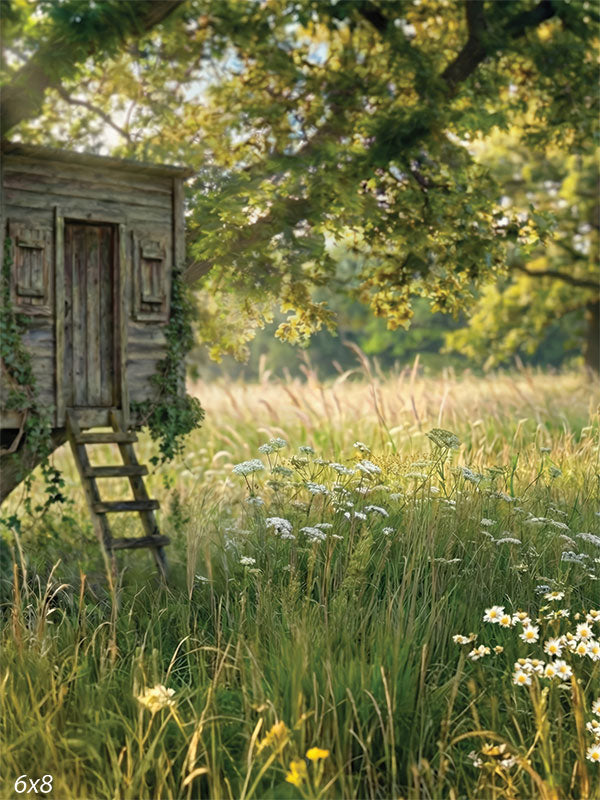 A photography backdrop showing a small weathered wooden treehouse beside a mature tree, surrounded by tall meadow grasses and wildflowers in soft natural light.
