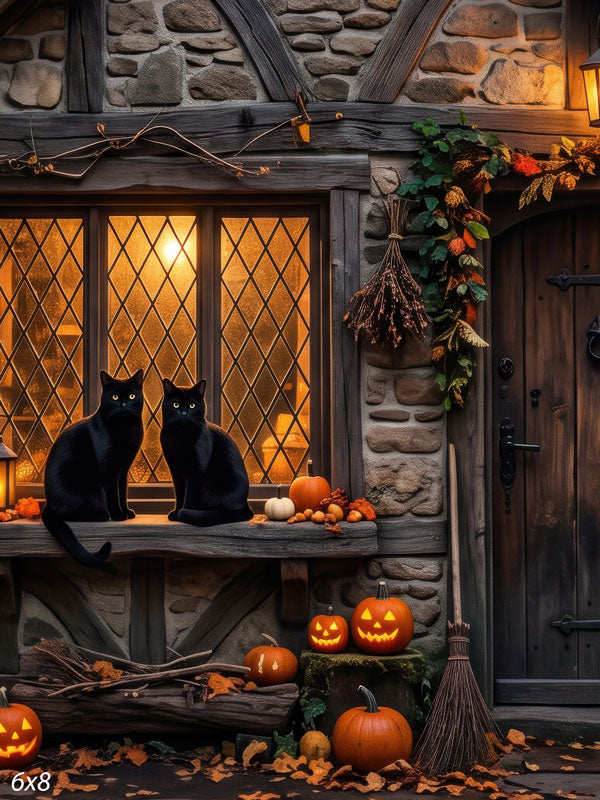 Two black cats on a glowing leaded cottage window in a stone-and-timber wall with autumn foliage, a broom, and jack-o'-lanterns, a Halloween photography backdrop.