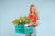 Smiling woman holding a crate of flowers against a light blue seamless photography backdrop paper in a professional studio.