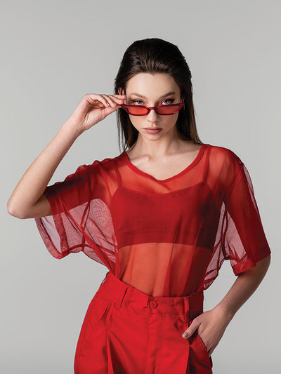 Female model wearing a red outfit posing against a light gray seamless photography backdrop paper in a studio setting.