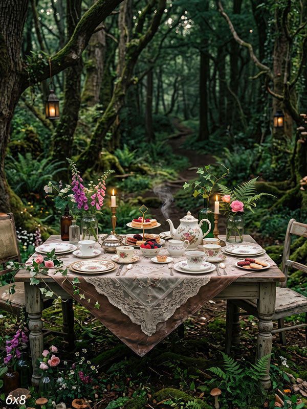 Storybook tea-party table with florals and candlelight set on a path in a mossy enchanted forest with hanging lanterns, a themed scenic photography backdrop.