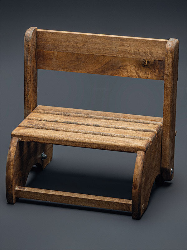 Wooden step stool bench photography prop with a slatted seat and curved sides, shown in an angled view set up as a bench with the backrest raised on a plain grey studio background.