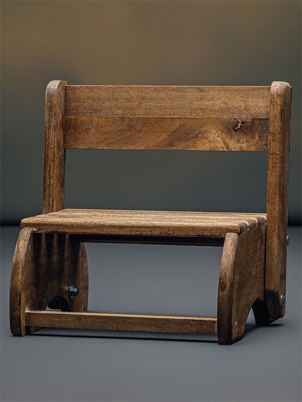 Wooden step stool bench photography prop with a slatted seat and curved sides, shown in a front view set up as a low bench with the backrest raised on a plain grey studio background.