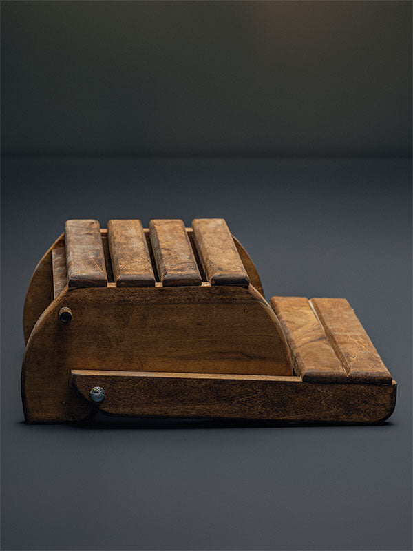Wooden step stool bench photography prop with a slatted seat and curved sides, shown in a side view showing the slatted top folded flat on a plain grey studio background.