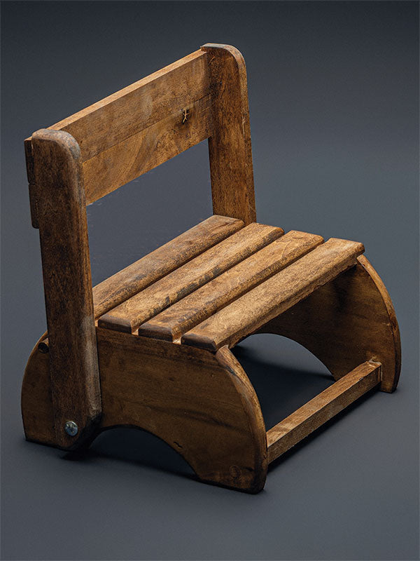 Wooden step stool bench photography prop with a slatted seat and curved sides, shown in a side view with the curved end panels visible on a plain grey studio background.