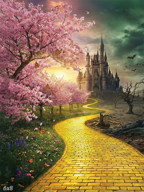 Photography backdrop showing a yellow brick pathway leading to a distant castle, with cherry blossom trees and wildflowers on one side and barren trees on the other under a dramatic sky.