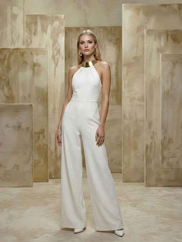 Blonde woman wearing a white sleeveless jumpsuit with a gold collar necklace stands upright against a beige abstract painted panel backdrop with tall rectangular forms.
