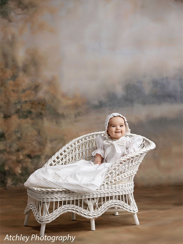 Ansel soft misty meadow with trees photography backdrop shown with a baby in a white heirloom gown and bonnet seated on a white wicker settee CP-8845