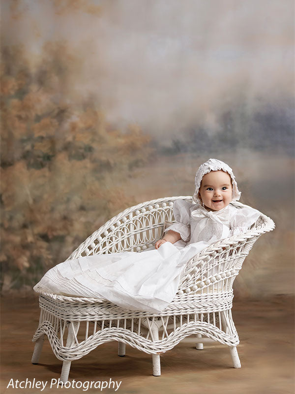 Ansel soft misty meadow with trees photography backdrop shown with a baby in a white heirloom gown and bonnet smiling on a white wicker settee CP-8845