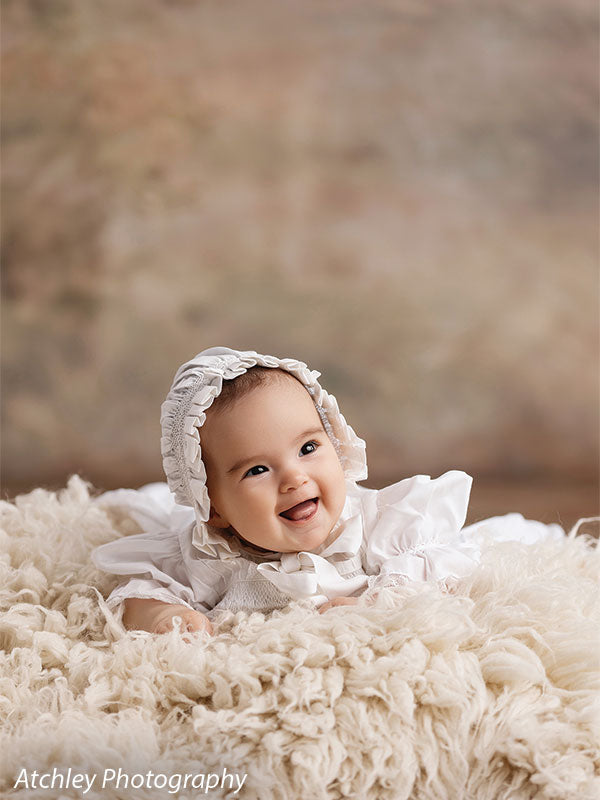 Ansel soft misty meadow with trees photography backdrop shown with a baby in a bonnet seated on a cream flokati fur rug CP-8845