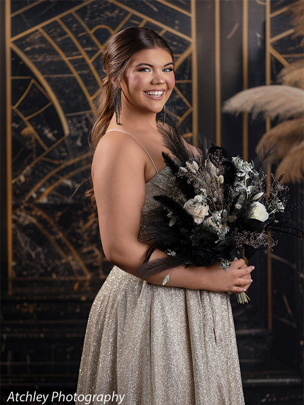 Elegant art deco black and gold photography backdrop featuring a young woman in a gold formal dress holding a dramatic bouquet, ideal for prom or formal event portraits.