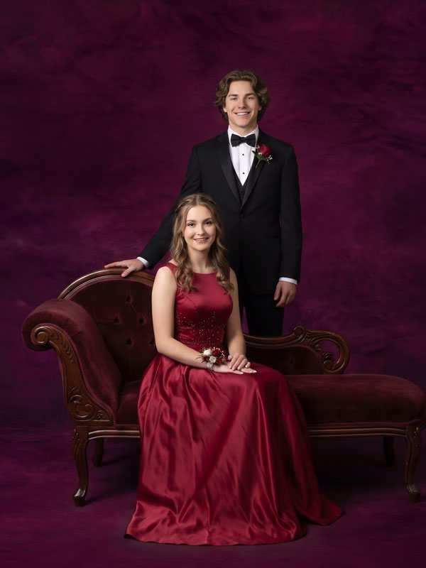 Aubergine Dusk deep plum mottled texture photography backdrop, shown with a prom couple, a young woman in a red gown seated on a fainting couch beside a young man in a tuxedo CP-9015