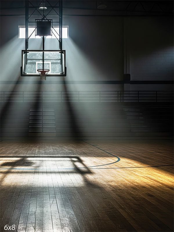 A spotlighted basketball hoop casts crisp shadows on a glossy hardwood floor in a quiet, empty gym.