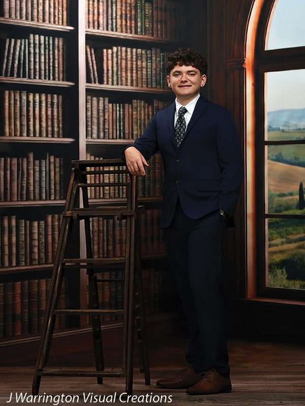 Benedict dark wood library bookcase photography backdrop shown with a senior in a navy suit standing beside a library ladder, smiling CP-8839