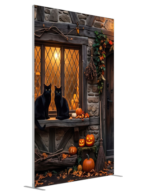 Two black cats on a glowing leaded cottage window in a stone-and-timber wall with jack-o'-lanterns, 5ft photography backdrop panel for Denny StudioEdge silicone edge frame, angled view