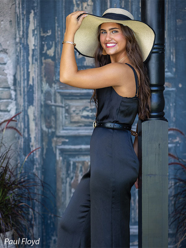 Black Ruin photography backdrop showing a weathered rustic door with peeling paint and an aged brick surround, shown with a senior girl in a black jumpsuit and sun hat turned to the side laughing CP-8789