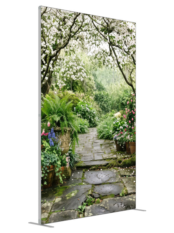 A stone garden path beneath blooming white dogwood trees with ferns, hostas and potted roses, 5ft photography backdrop panel for Denny StudioEdge silicone edge frame, angled view