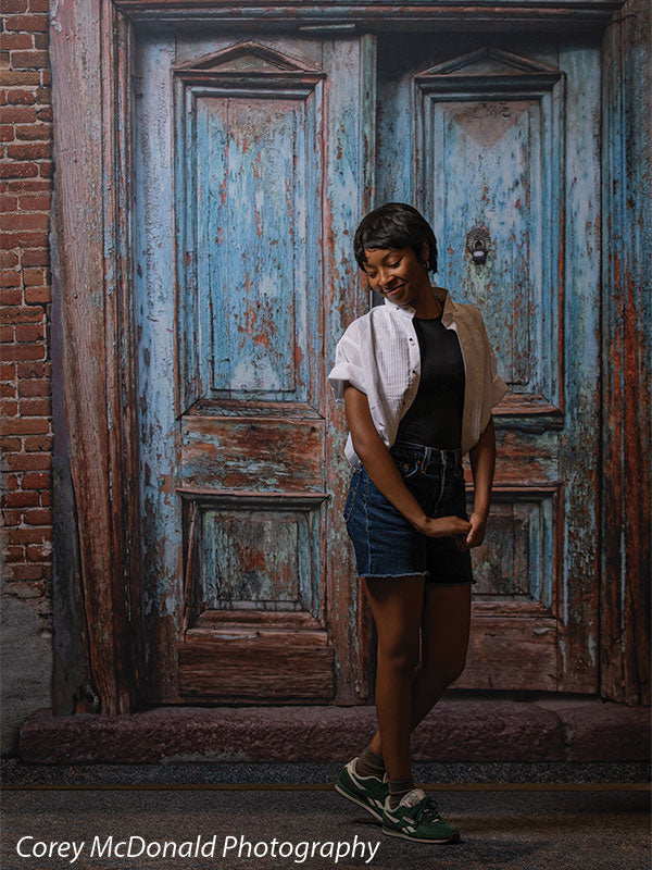 Blue Desire Street, photography backdrop panel for Denny StudioEdge silicone edge frame, shown with a senior girl standing full-length looking down beside the weathered door SECP-7654