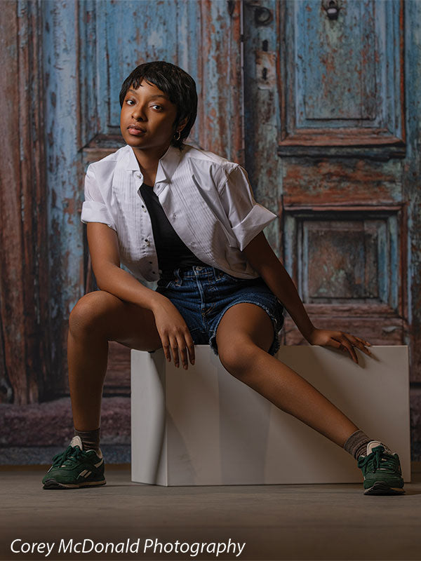 Blue Desire Street, photography backdrop panel for Denny StudioEdge silicone edge frame, shown with a senior girl seated on a white posing cube beside the weathered door SECP-7654