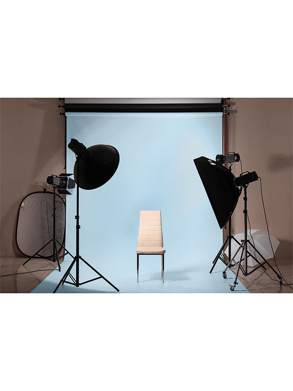 Professional studio setup with soft lighting equipment and a light blue seamless paper backdrop, showcasing a neutral chair for product or portrait photography.