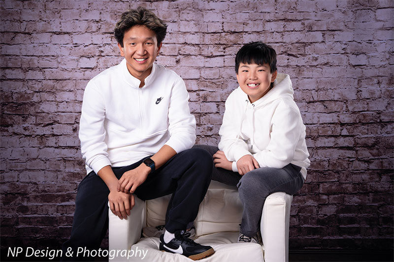 Broadway Brick exposed brick photography backdrop shown with two brothers by the brick wall, one seated and one standing, wide view CP-7742