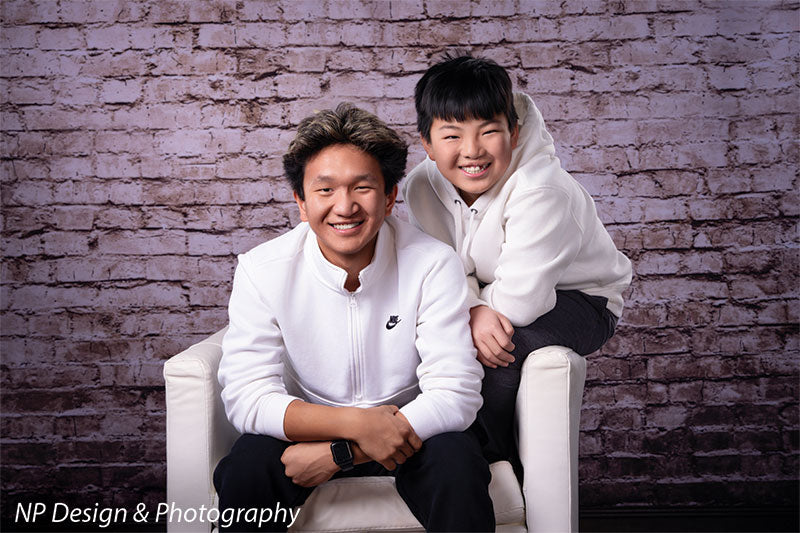 Broadway Brick exposed brick photography backdrop shown with two brothers seated together by the brick wall, wide view CP-7742