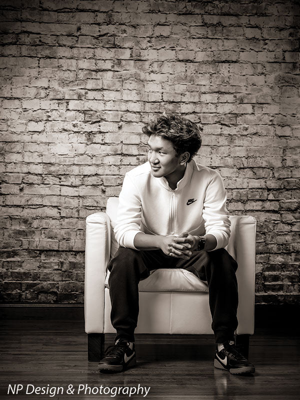 Broadway Brick exposed brick photography backdrop shown with a senior boy seated in a white armchair under dramatic side light CP-7742