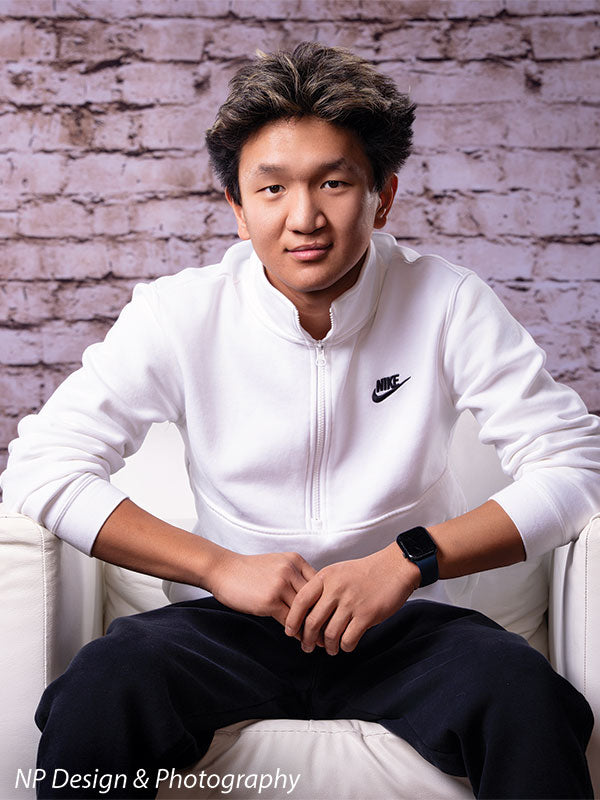 Broadway Brick exposed brick photography backdrop shown with a senior boy in a white quarter-zip seated in a white armchair, close portrait CP-7742
