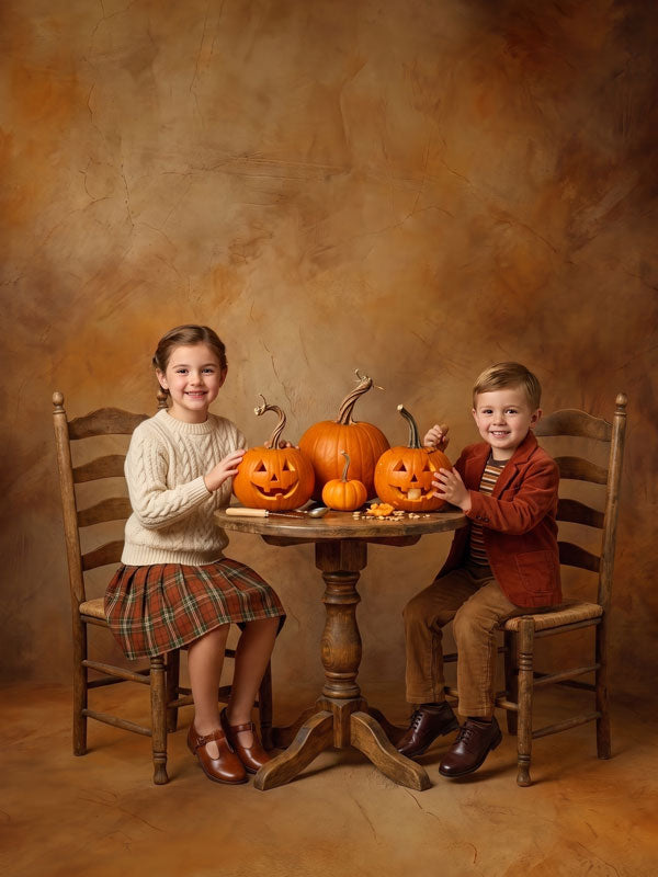 Burnt Honey warm amber mottled texture photography backdrop shown with two young children in cream sweaters at a round table of carved pumpkins in an autumn setup CP-9024