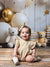 Close-up of a toddler girl sitting in front of white and gold balloons and teddy bears on the Bears and Stars Cake Smash Backdrop.