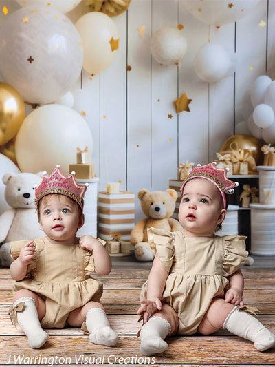 Twin girls wearing birthday crowns seated in front of gold star balloons and teddy bears on the Bears and Stars Cake Smash Backdrop.