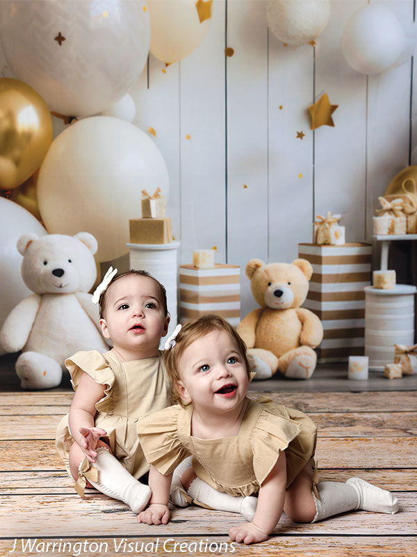 Twin toddlers crawling on a rustic wood floor with gold and white balloons, teddy bears, and presents in the Bears and Stars Cake Smash Backdrop setup.